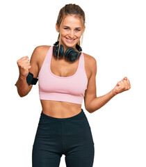Young blonde woman wearing gym clothes and using headphones excited for success with arms raised and eyes closed celebrating victory smiling. winner concept.
