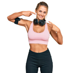 Young blonde woman wearing gym clothes and using headphones smiling cheerful showing and pointing with fingers teeth and mouth. dental health concept.