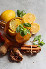 Glass teapot with ginger tea, lemon, turmeric root and mint on grey background with space for text. Cold and flu season concept. 