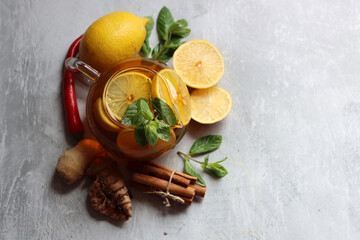 Glass teapot with ginger tea, lemon, turmeric root and mint on grey background with space for text. Cold and flu season concept. 