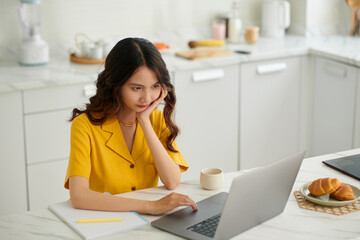 Bored university student sitting at kitchen counter when attending online class