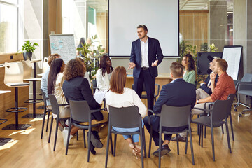 Business meeting. Serious business group leader instructing team, telling project strategy and presenting tasks. Confident man is talking to colleagues sitting in circle at meeting in office.
