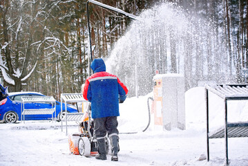 Man with petrol snow blower clearing snow and ice on parking area. Worker removing snow with...