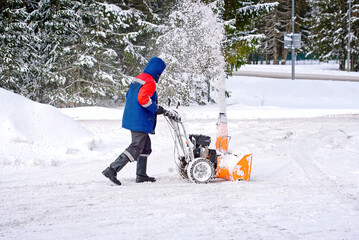 Man with petrol snow blower clearing snow and ice on parking area. Worker removing snow with...