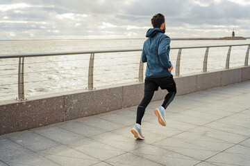 Man jogging by the sea during sunset, active lifestyle.