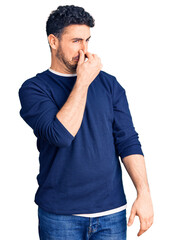 Young hispanic man wearing casual clothes smelling something stinky and disgusting, intolerable...