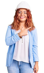 Young latin woman wearing architect hardhat cheerful with a smile of face pointing with hand and finger up to the side with happy and natural expression on face