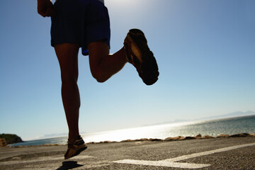 Person, running and asphalt at beach for fitness, workout or outdoor cardio training on a sunny...