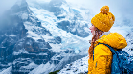 Eine Frau in gelber Mütze und Jacke wandert durch verschneite Bergen.
