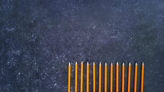 Pencils on a dark background. Stop motion animation. Orange graphite pencils appear and disappear one by one. Back to school. Business, paperwork, study concept.
