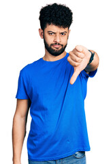 Young arab man with beard wearing casual blue t shirt looking unhappy and angry showing rejection and negative with thumbs down gesture. bad expression.