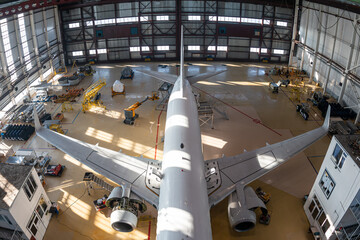 Top view of a white passenger jet plane in the aviation hangar. Airliner under maintenance....