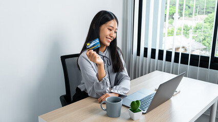 Young asian woman holding credit card and looking on laptop to using for online shopping