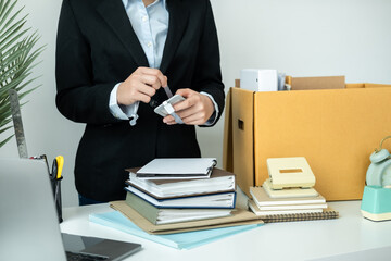 Business woman employee in suit packing id card of office worker and personal belongings into brown cardboard box
