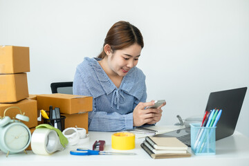 Asian woman small business owner holding smartphone to receive and checking order from customer while working
