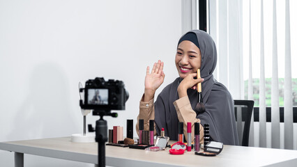 Asian muslim woman beauty blogger holding makeup brush to tutorial how to use cosmetic in front of...