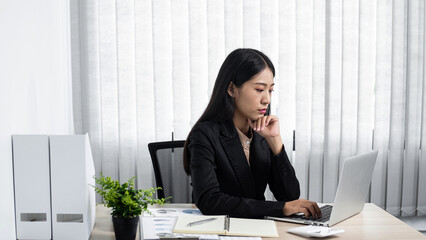 Young secretary woman thinking with hand on chin surrounded about too much work and using laptop