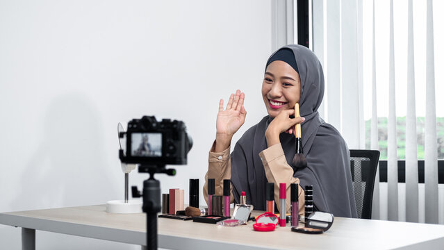Asian muslim woman beauty blogger holding makeup brush to tutorial how to use cosmetic in front of camera
