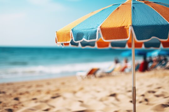 Close up image of a yellow and blue beach umbrella on a background of a beach with sun loungers and blue sea