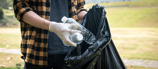 Volunteer man in gloves standing to picking up plastic bottle into plastic black bag for cleaning the park
