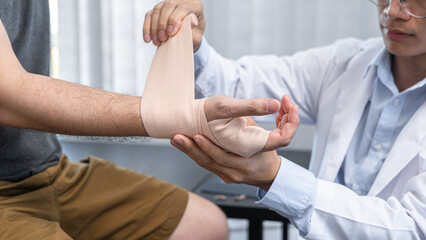 Young asian physiotherapist bandaging hand of man patient with in injury