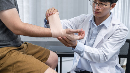 Young asian physiotherapist bandaging hand of man patient with in injury