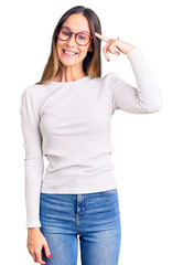 Beautiful brunette young woman wearing casual white sweater and glasses smiling pointing to head with one finger, great idea or thought, good memory