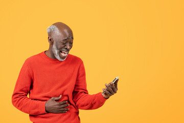 Joyful elderly man in a red sweater laughs while looking at a smartphone