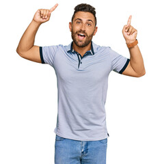 Handsome man with beard wearing casual clothes smiling amazed and surprised and pointing up with fingers and raised arms.