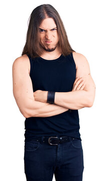 Young adult man with long hair wearing goth style with black clothes skeptic and nervous, disapproving expression on face with crossed arms. negative person.