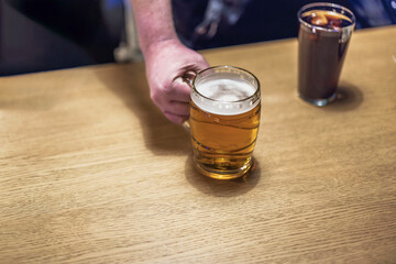 View of a male hand picking up a mug of beer from the table in a bar.