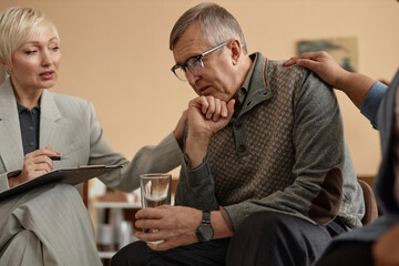 Side view portrait of senior man sharing mental health trouble with people comforting him during group therapy session