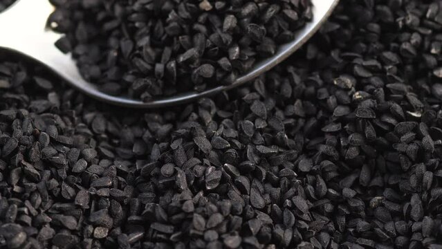 spoon in a pile of black cumin seeds rotation. macro black cumin seeds.asian spices.black cumin harvest
