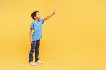 Curious boy reaching out free space in blue shirt on yellow background