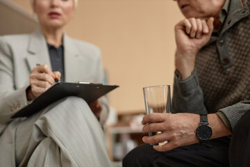 Side view closeup of senior man holding glass of water and talking to psychologist in therapy session, copy space