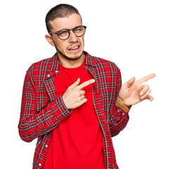 Hispanic young man wearing casual clothes pointing aside worried and nervous with both hands,...