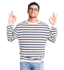 Hispanic handsome young man wearing casual clothes and glasses relax and smiling with eyes closed doing meditation gesture with fingers. yoga concept.