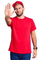 Young handsome blond man wearing t-shirt and cap doing stop sing with palm of the hand. warning expression with negative and serious gesture on the face.