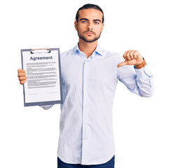 Young handsome man holding clipboard with agreement document with angry face, negative sign showing...