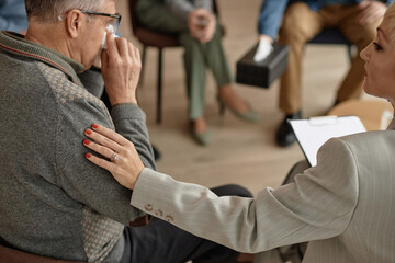 Close up of caring female therapist comforting senior man in group therapy session and putting hand on shoulder