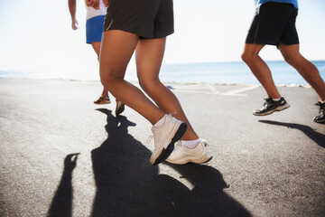People, team and legs running at beach for cardio, fitness or outdoor workout together on asphalt...