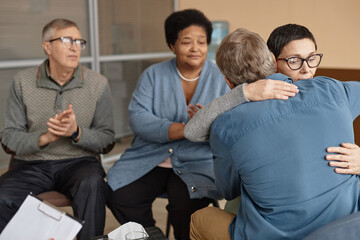 Back view of two senior people embracing in group therapy session supporting each other with mental health struggles, copy space - Powered by Adobe