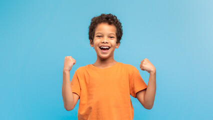 Exuberant boy in orange shirt, fists raised, blue background