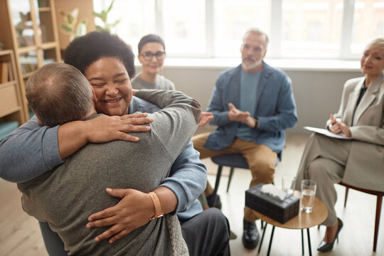 Portrait of Black senior woman embracing friend in group therapy session and smiling happily celebrating recovery, copy space