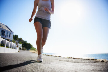 Woman, running and asphalt at beach for fitness, workout or outdoor cardio training on a sunny day....