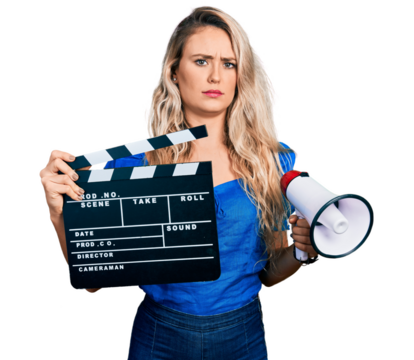 Young blonde woman holding video film clapboard and megaphone skeptic and nervous, frowning upset because of problem. negative person.