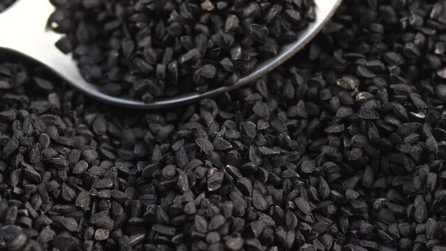 close-up black cumin seeds heap in a spoon rotation. slow motion. macro heap of black cumin seeds. healthy ingredients asian spices
