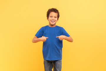 Happy boy pointing at himself with thumbs on yellow background