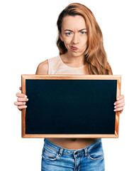 Young caucasian woman holding blackboard skeptic and nervous, frowning upset because of problem....