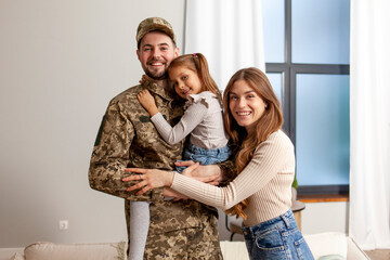 Fototapeta na wymiar young soldier of the Ukrainian army in a camouflage uniform returned home to his family, a military dad hugs his little daughter and wife at home